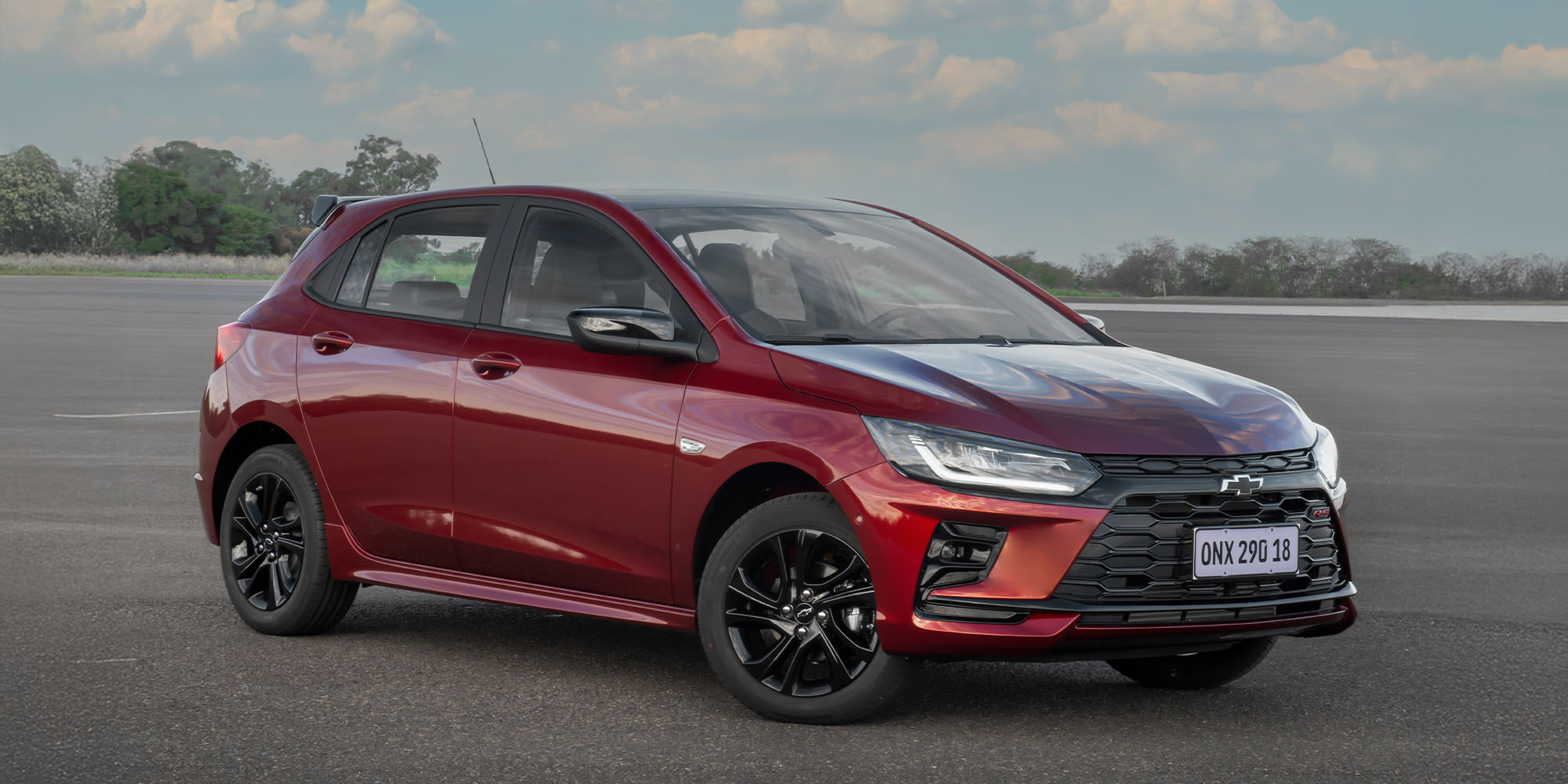 Chevrolet Onix rojo estacionado en un espacio abierto.